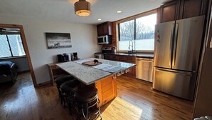 A modern kitchen with a central island, wooden cabinets, a stainless steel refrigerator, and a window providing natural light.
