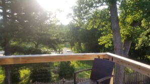 A wooden deck with a chair, overlooking a pond and trees.