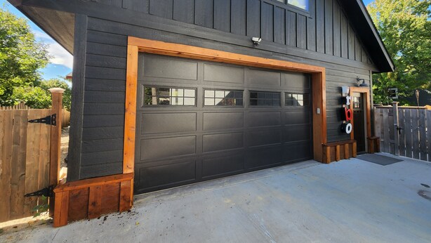 A modern two-story house with a dark grey exterior, a large garage door, and a wooden deck.