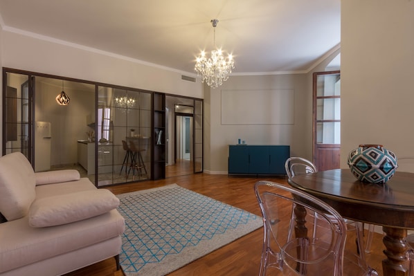 Una sala de estar moderna con sofá, mesa de comedor, candelabro y alfombra estampada.