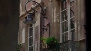 A building facade with ornate iron balcony railings, a street lamp, and a window with a plant on the balcony. - Suite 101 - Cagliari (Cagliari)