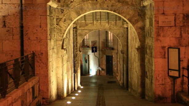An arched stone corridor with a tiled floor, a metal railing on the left, and a sign on the right. - Suite 101 - Cagliari (Cagliari)