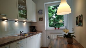 Uma cozinha moderna com armários brancos, bancada de madeira e uma cafeteira. Há uma janela com vista para o verde lá fora.
