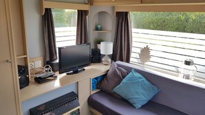 A cozy RV interior with a TV, remote controls, a lamp, and a sofa with a patterned pillow. - Mobile Home in Renesse at the 4-star Camping de Brem (Renesse)
