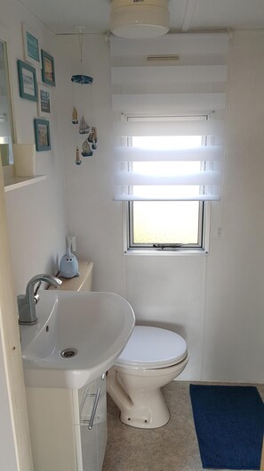 A small, clean bathroom with a toilet, sink, and window. - Mobile Home in Renesse at the 4-star Camping de Brem (Renesse)