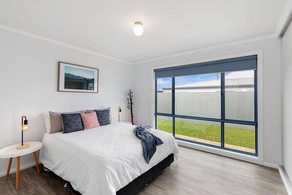 A bedroom with a large window, a bed, a bedside table, and a picture on the wall. - The Kingfisher - Family friendly, centrally located near Robes main street. (Robe)