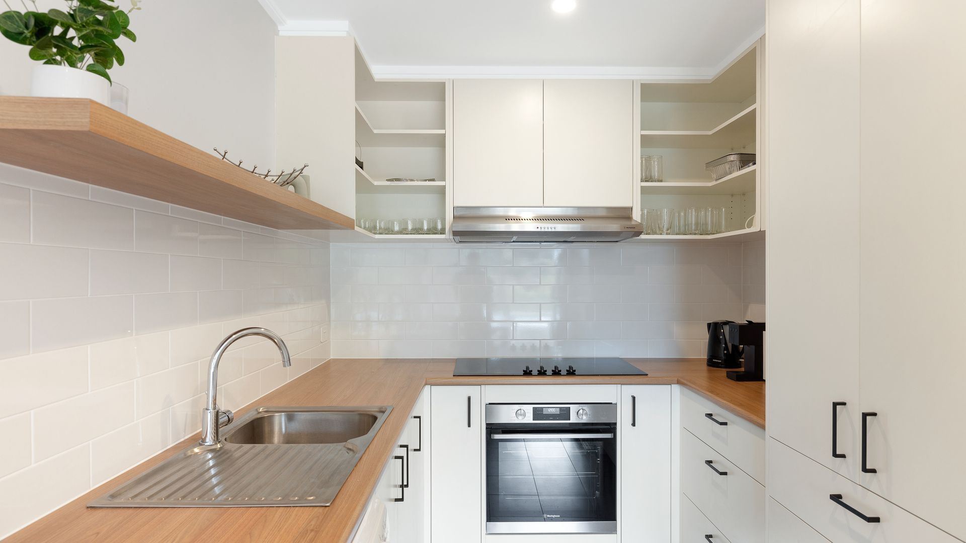 A modern kitchen with a stainless steel sink, a built-in oven, and white cabinetry.