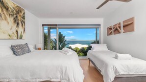 Ein Schlafzimmer mit zwei Betten, einem großen Fenster mit Meerblick und einem Deckenventilator.