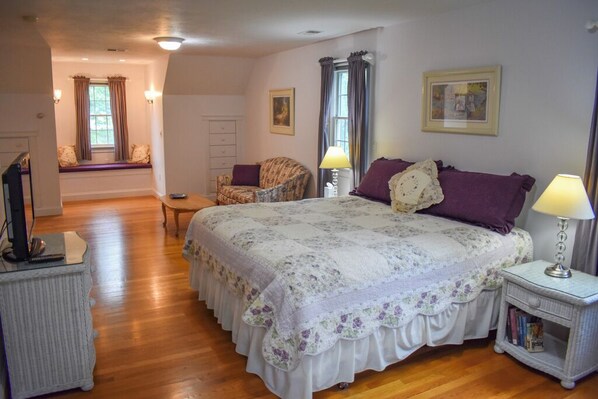 A bedroom with a large bed, a chair, a small table, and a window with curtains.