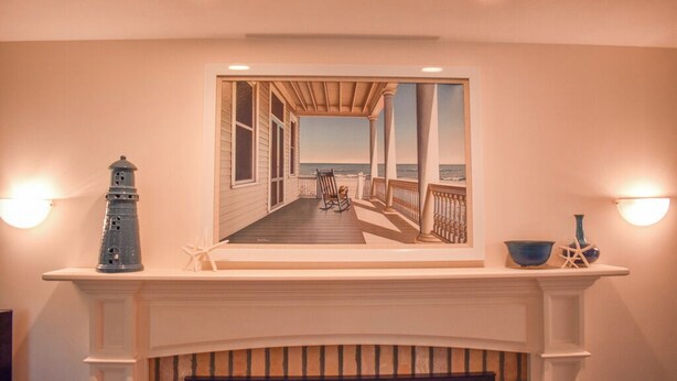 A fireplace with a coastal scene painting above it, a lighthouse, and a starfish decoration.