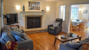 A living room with a fireplace, a television, and a dining area with wooden chairs and a table.