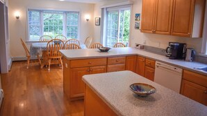 A kitchen with wooden cabinets, a granite countertop, and a dishwasher. There are two windows providing natural light.