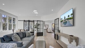 Una sala moderna con un sofá gris, sillones estampados, un banco de madera y un ventanal grande.