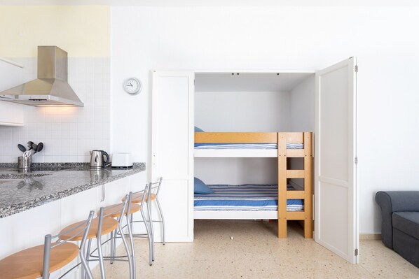 Una habitación compacta con kitchenette, una litera, una pequeña barra y una zona de estar.