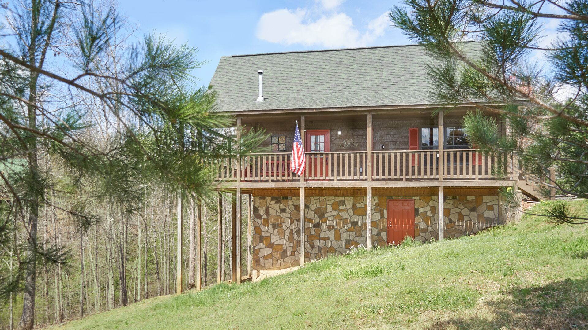 Eine zweistöckige Holzhütte mit Steinfassade, einem Balkon mit Geländer und einer amerikanischen Flagge.