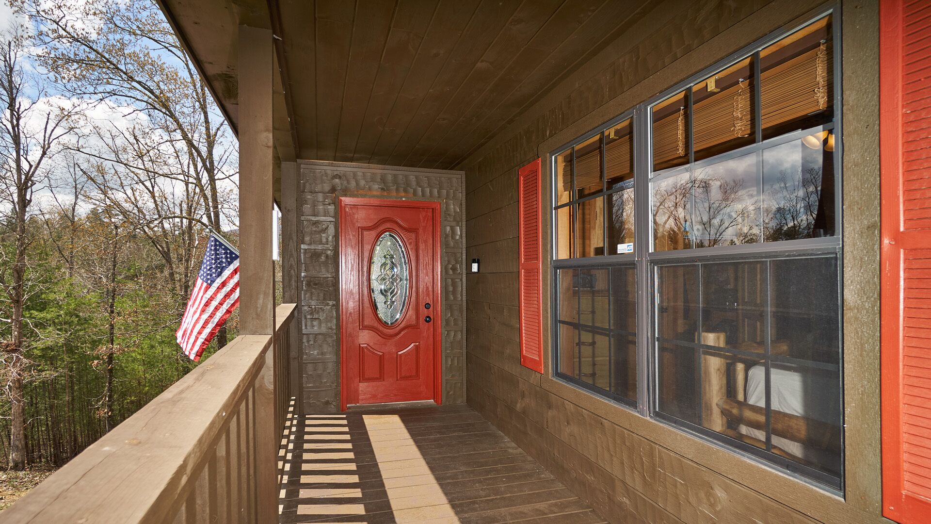 A covered porch with a red door, large windows with shutters, and an American flag.