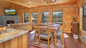 A cozy cabin interior with a fireplace, dining area, and large windows offering views of the outdoors. - Best Price!!! Cabin with Mountain Views, Hot Tub, Sleeps 6, 10 Min to Parkway! (Sevierville)
