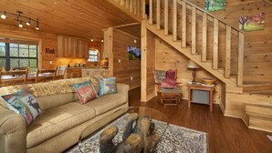 A cozy cabin interior with a wooden staircase, a sofa with patterned cushions, and a dining area with wooden cabinets. - Best Price!!! Cabin with Mountain Views, Hot Tub, Sleeps 6, 10 Min to Parkway! (Sevierville)