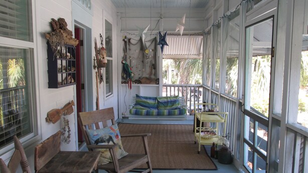 Eine gemütliche Veranda mit Holzmöbeln, einem Schaukelstuhl und einem farbenfrohen Sofa.