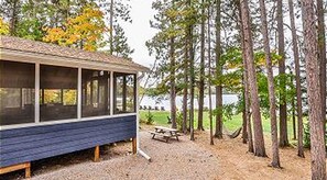 A cabin with a covered porch, a picnic table, and a forested area in the background.