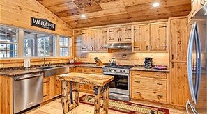 A wooden cabin-style kitchen with a 'WELCOME' sign, wooden cabinets, a stainless steel refrigerator, and a central island.