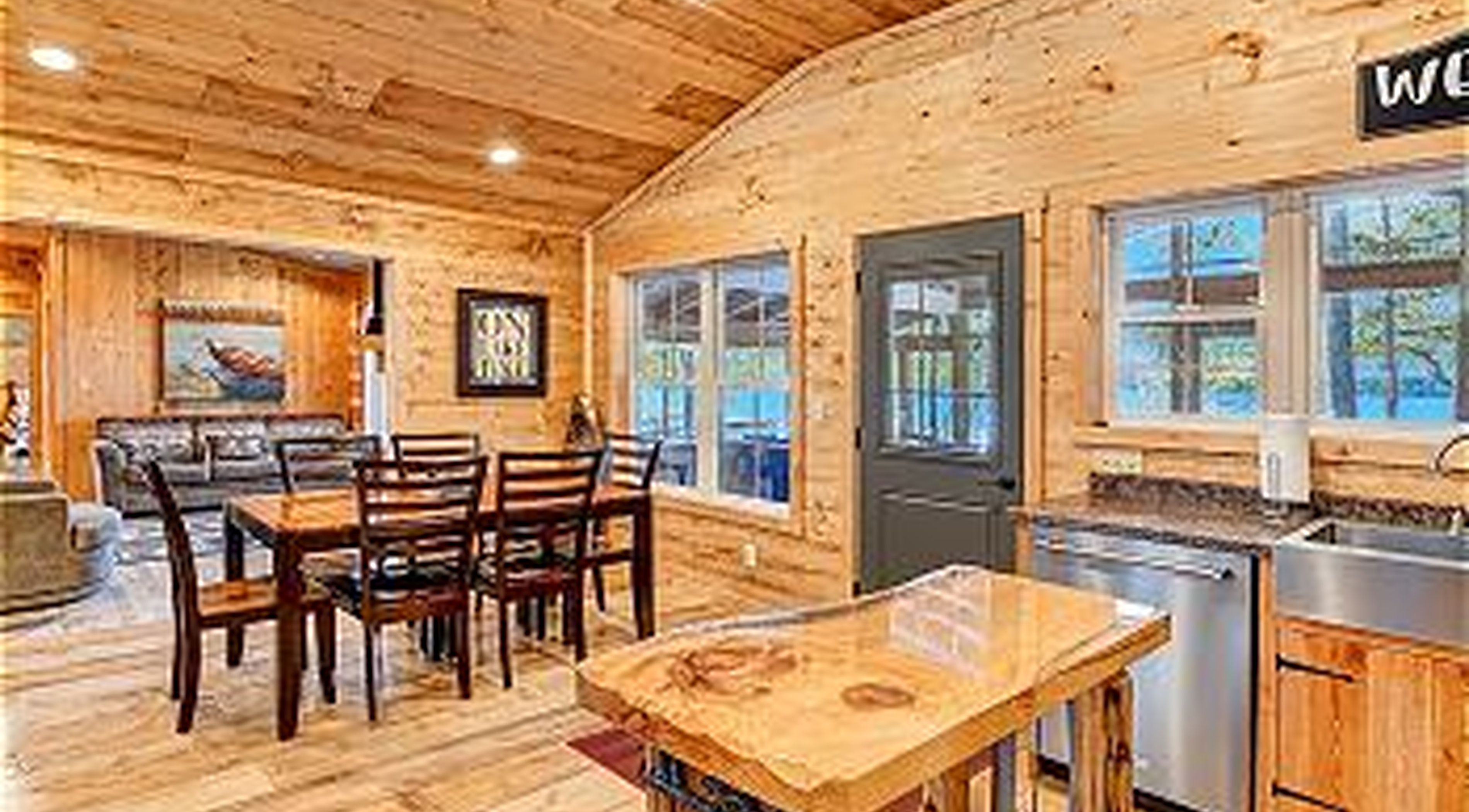 A wooden cabin interior with a dining area, kitchen, and a door leading outside.