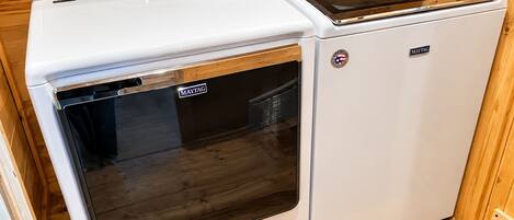 Een witte wasmachine en droger van Maytag, met bedieningspaneel en deur van roestvrij staal, in een kamer met houten lambrisering.