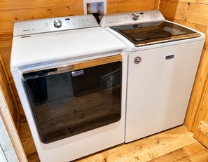 Et hvidt Maytag vaske- og tørresæt med kontrolpanel og en dør i rustfrit stål, installeret i et rum med træpaneler.