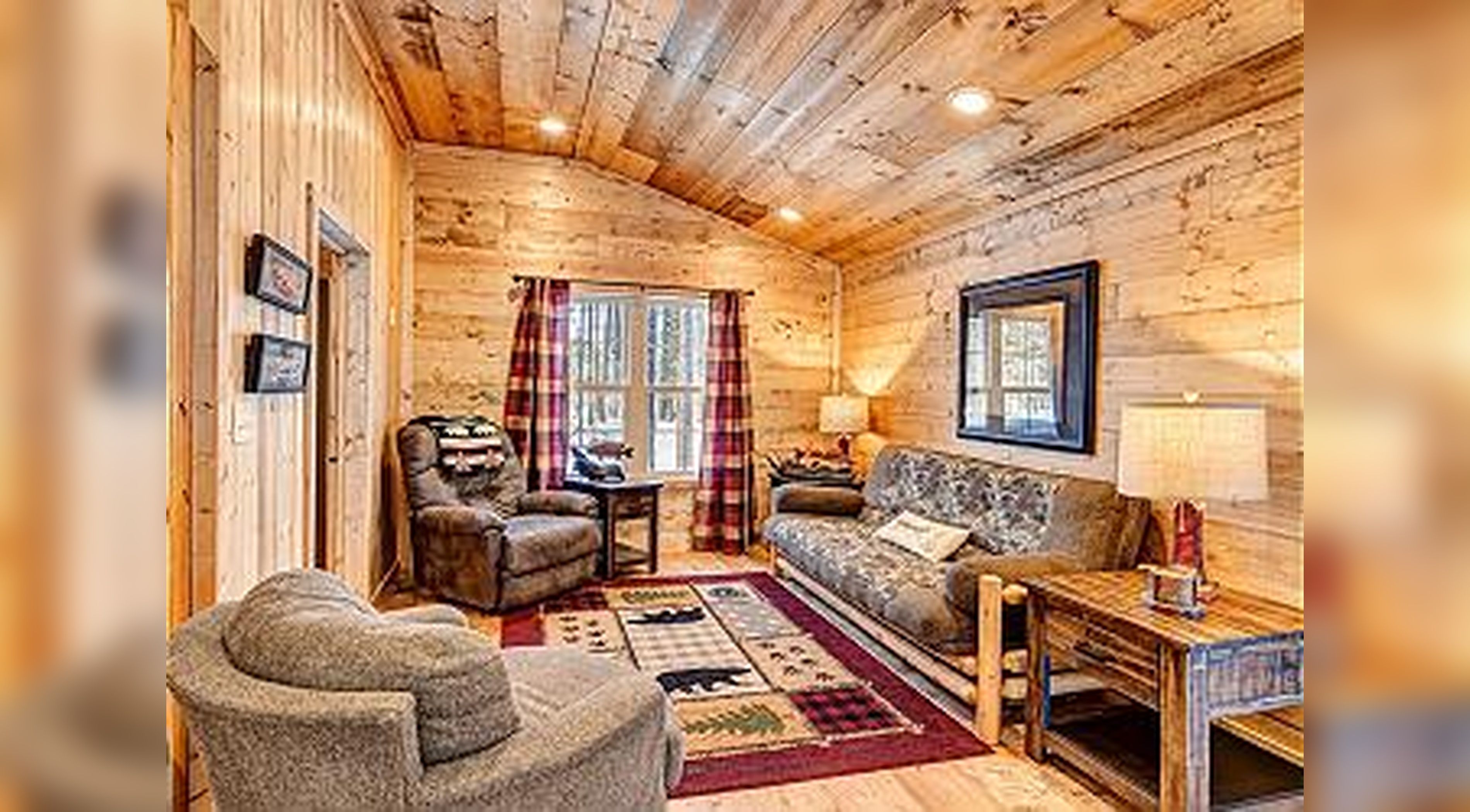 A cozy log cabin interior with a fireplace, a sofa, a chair, and a rug.