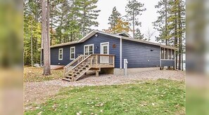 A two-story cabin with a wooden staircase leading to a porch, surrounded by trees.