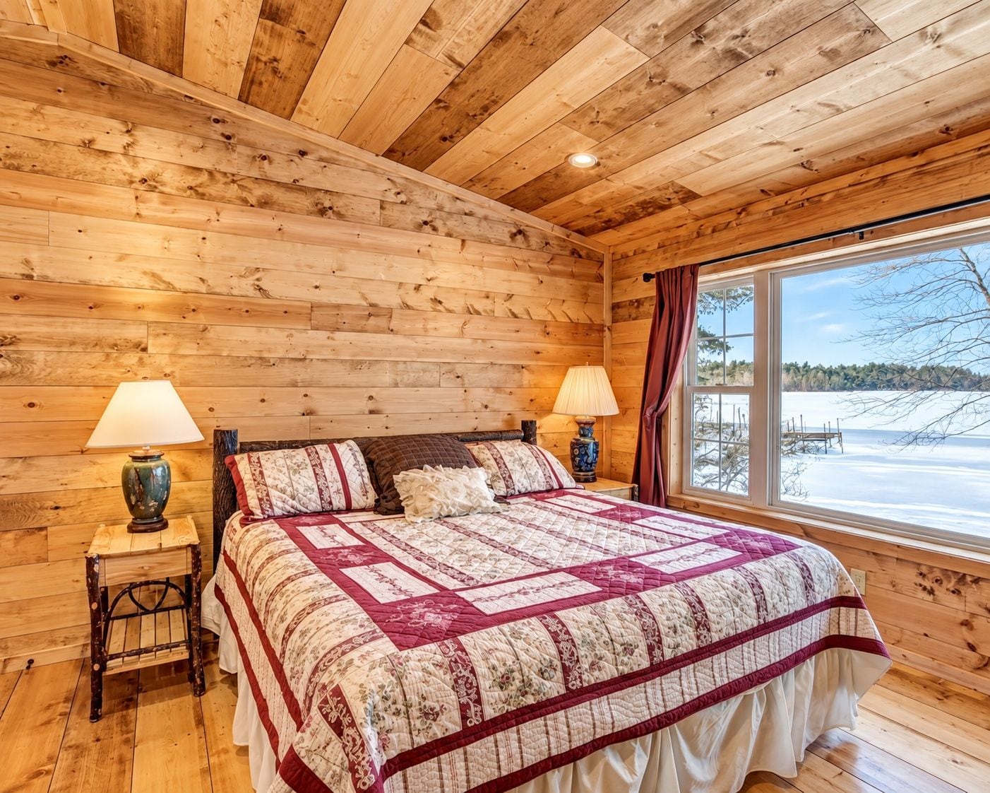 Un dormitorio de cabaña de madera con una cama grande, dos lámparas de noche y un ventanal con vistas a un paisaje nevado.