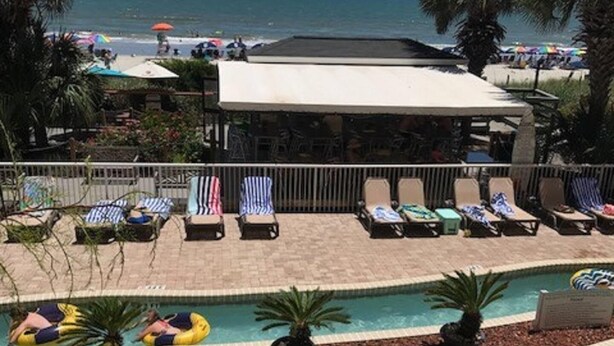 A pool area with lounge chairs and inflatable rafts, a covered seating area, and a view of the ocean. - Partial View 2 BR 2 BA, 7/3/26 to 7/10/26, Week 27, Fri-Fri, Room #1501 (North Myrtle Beach)