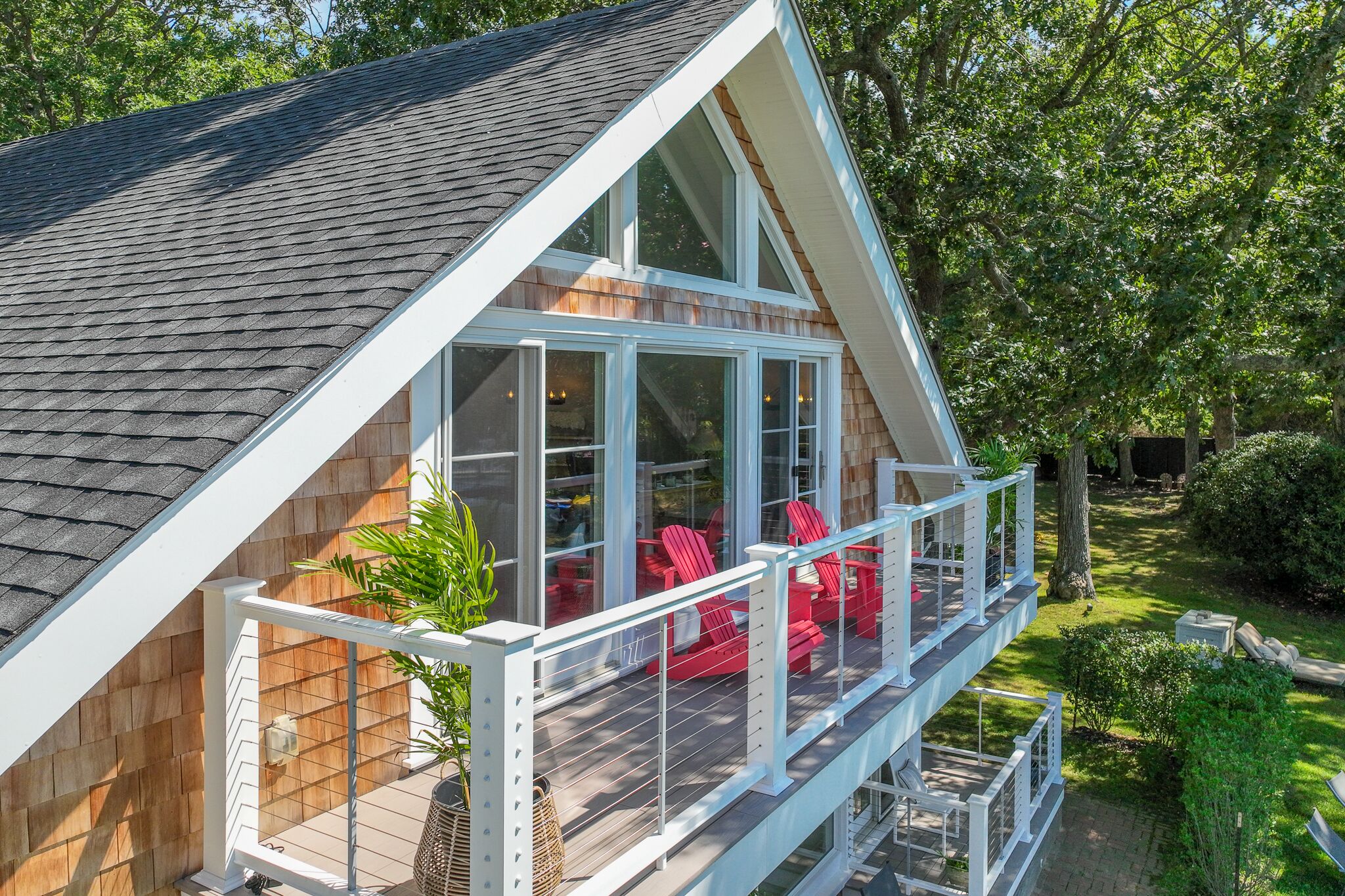 Ett modernt hus med ett stort glasfönster, en träveranda och röda utemöbler.