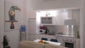 A compact kitchen with a refrigerator, microwave, and dishwasher. A dining table with fruits is in the foreground. - Beachside apartment (Santander)