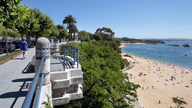 A coastal promenade with a stone balustrade, a beach with people, and boats in the water. - Beachside apartment (Santander)