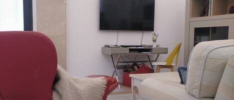 Ein modernes Wohnzimmer mit einem an der Wand montierten Flachbildfernseher, einem roten Sessel, einem weißen Sofa und einem Holztisch.