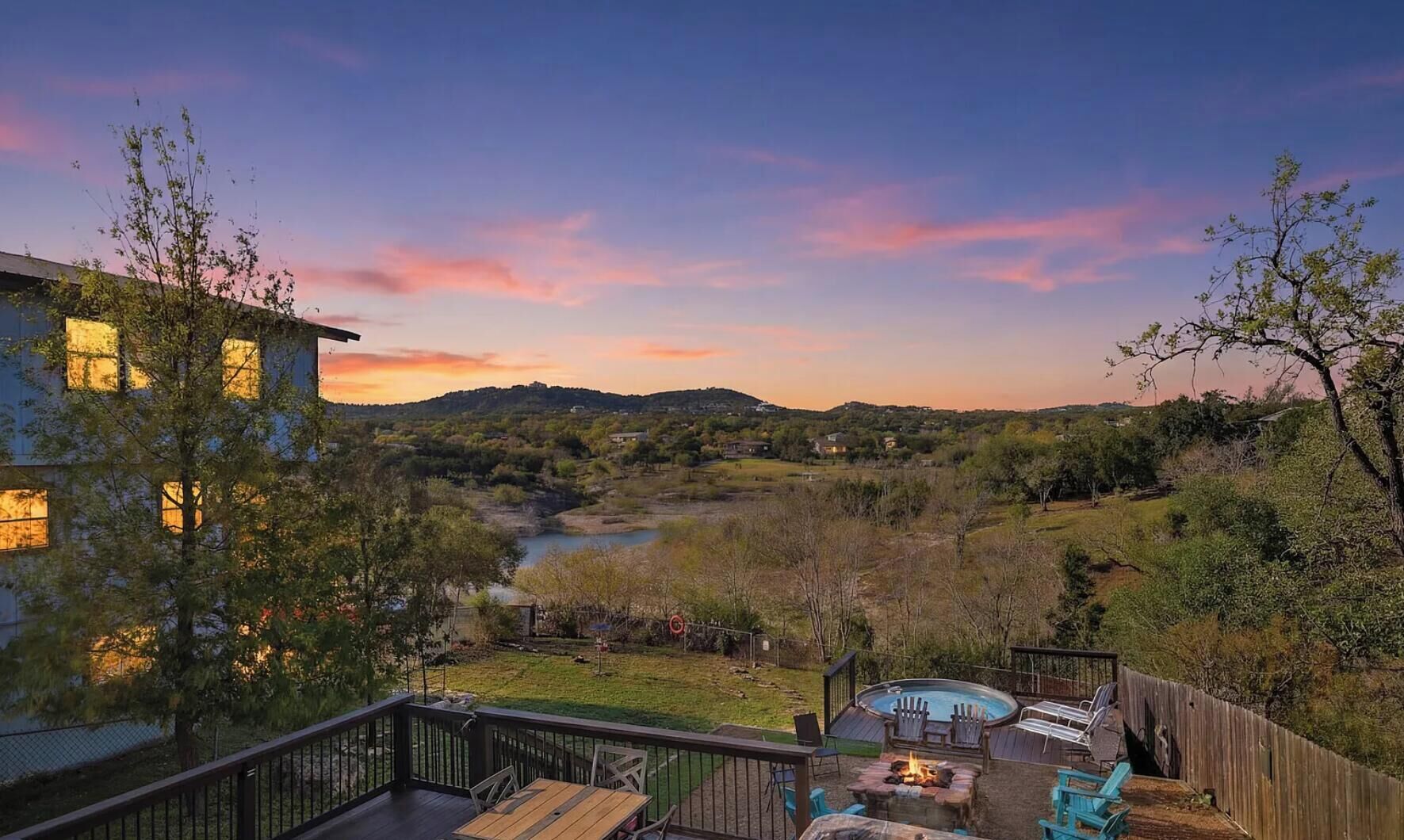 A deck with outdoor seating and a fire pit, overlooking a river and hills.