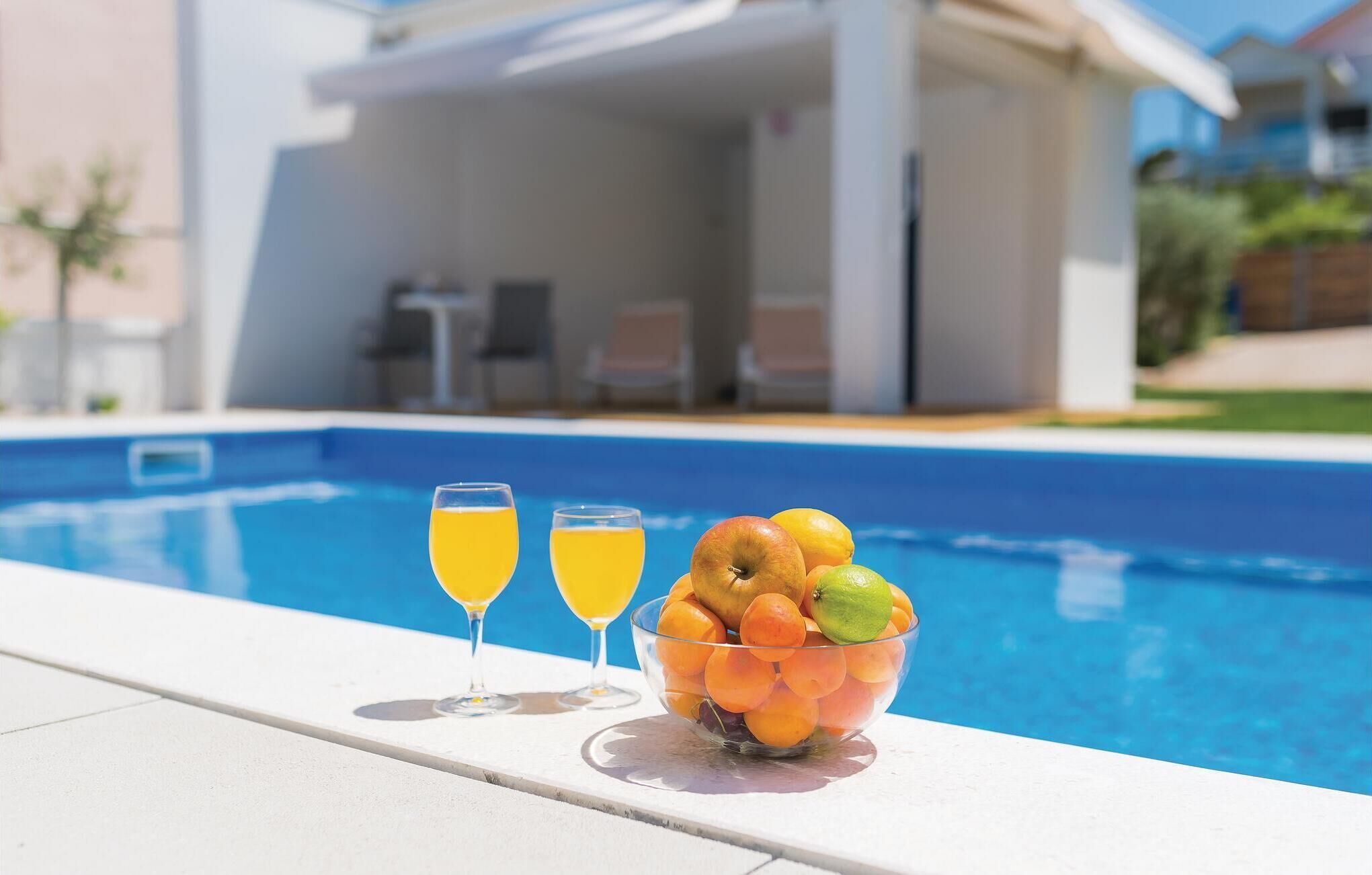Ein Poolbereich mit klarem, blauem Pool, zwei Orangensaftgläsern und einer Obstschale.