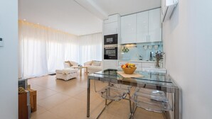 Een moderne keuken met een glazen eettafel, witte kasten en een ingebouwde oven.