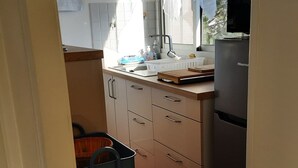 Pieni, käytännöllinen keittiö, jossa on pesuallas, jääkaappi ja punaisella tyynyllä varustettu tuoli.