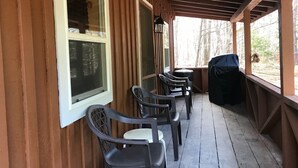 Une véranda couverte avec des murs en bois et un sol carrelé, comprenant des chaises en plastique et un barbecue.