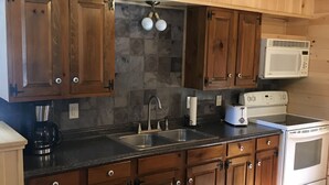Une cuisine avec des meubles en bois, un plan de travail en granit, un évier, une cuisinière et un four à micro-ondes.