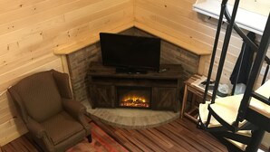 L’intérieur d’un chalet confortable, avec une cheminée, un téléviseur, un fauteuil et un tapis en peau de cerf.