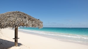 A beach with a thatched umbrella and a clear view of the ocean. - Lux Beachfront House W/ Private Pool on Banks Rd. Walk to Tippy's! (Governors Harbour)
