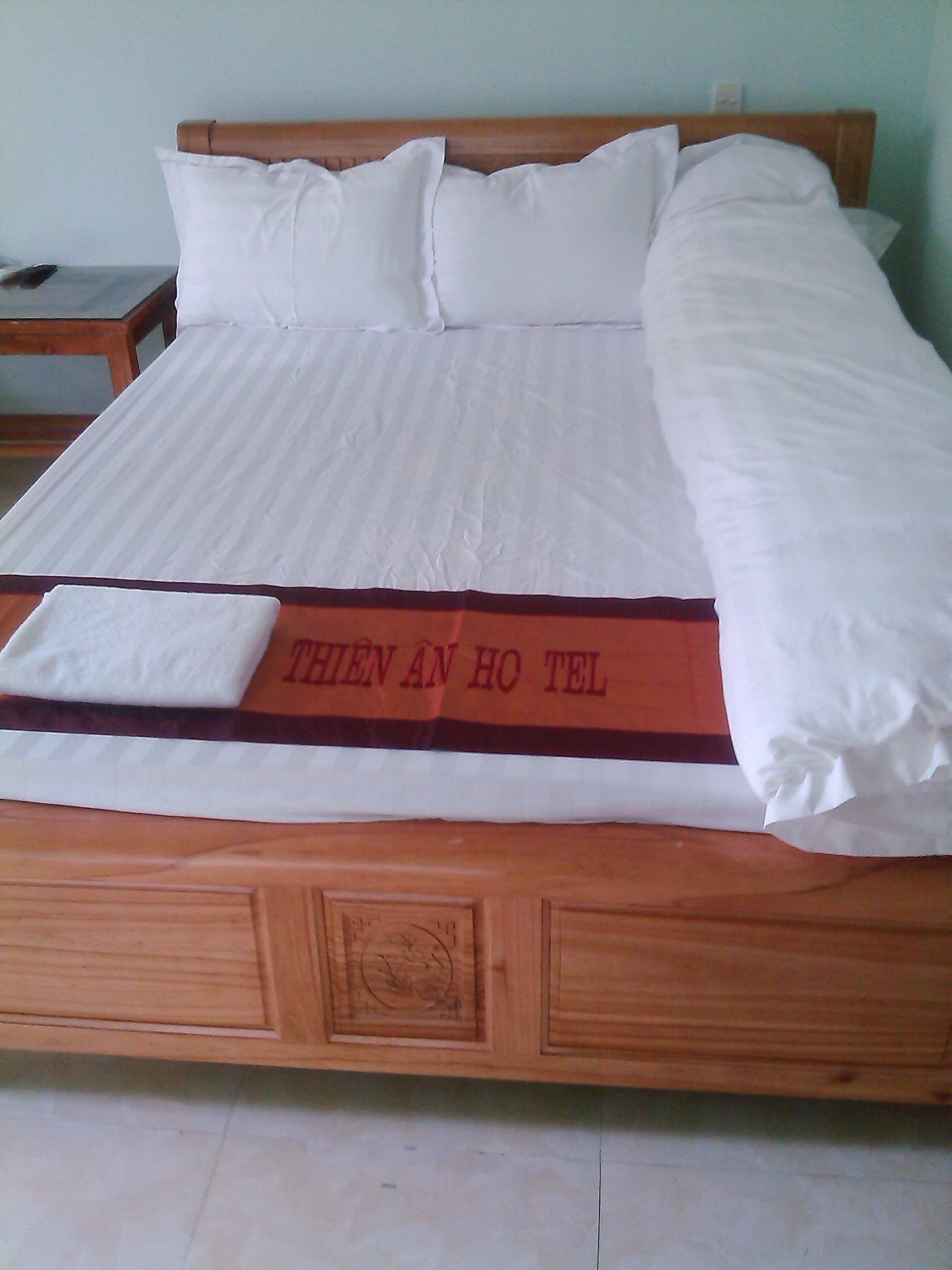 A wooden bed with white bedding and a red and white blanket with text.