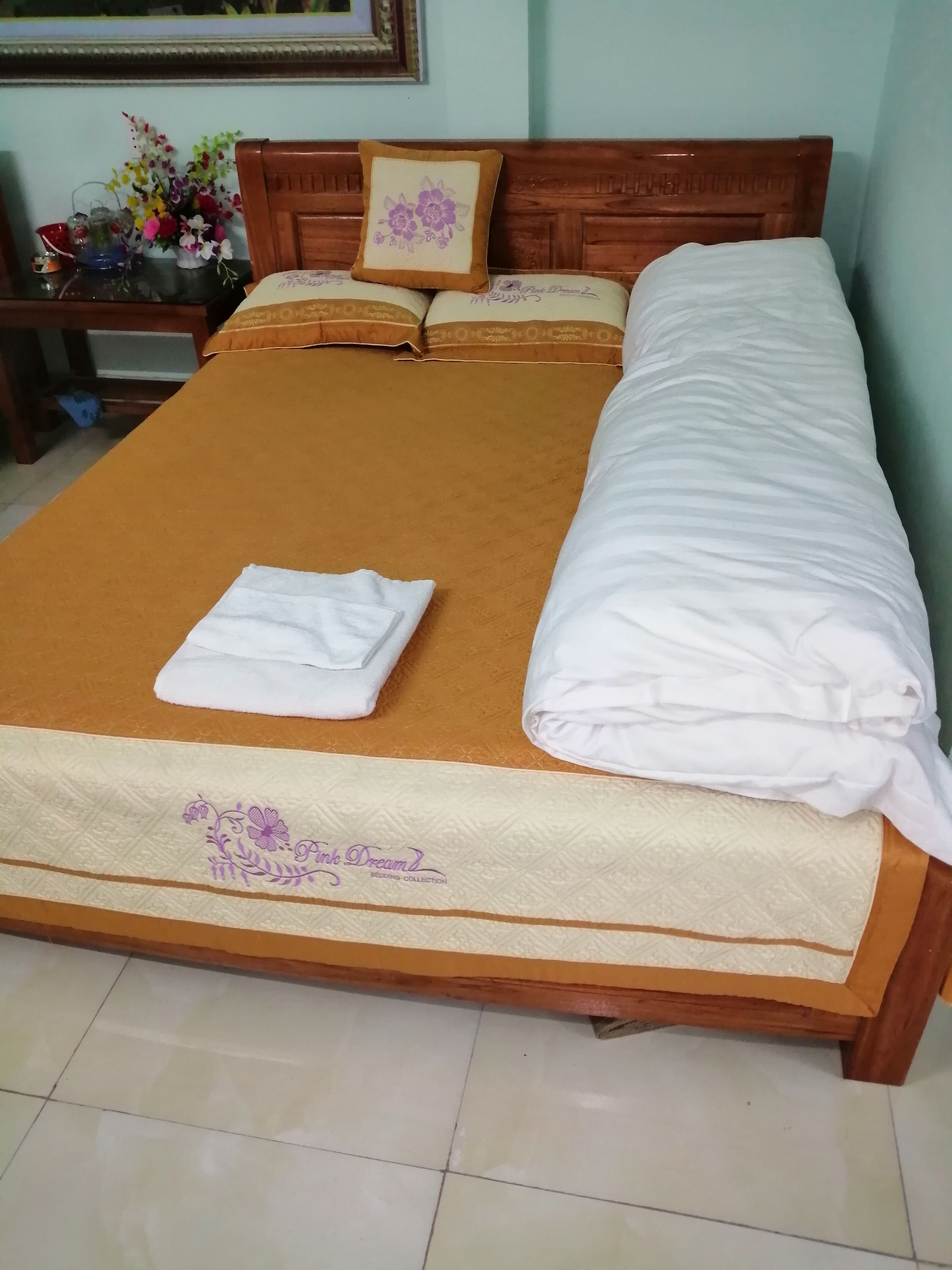 A neatly made bed with a brown bedspread and white linens, including a folded towel and a rolled-up blanket.