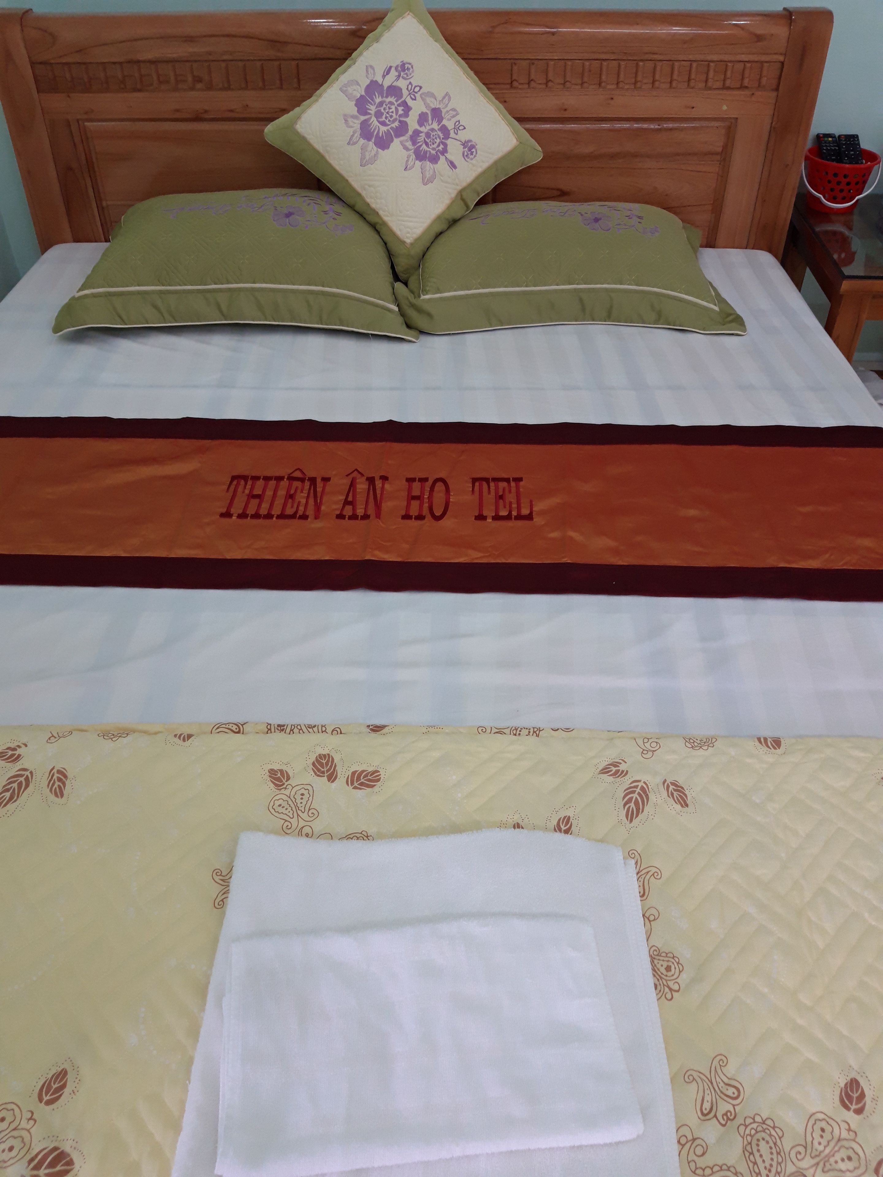 A bed with a floral pillow, a bedspread with a text banner, and a neatly folded white towel.