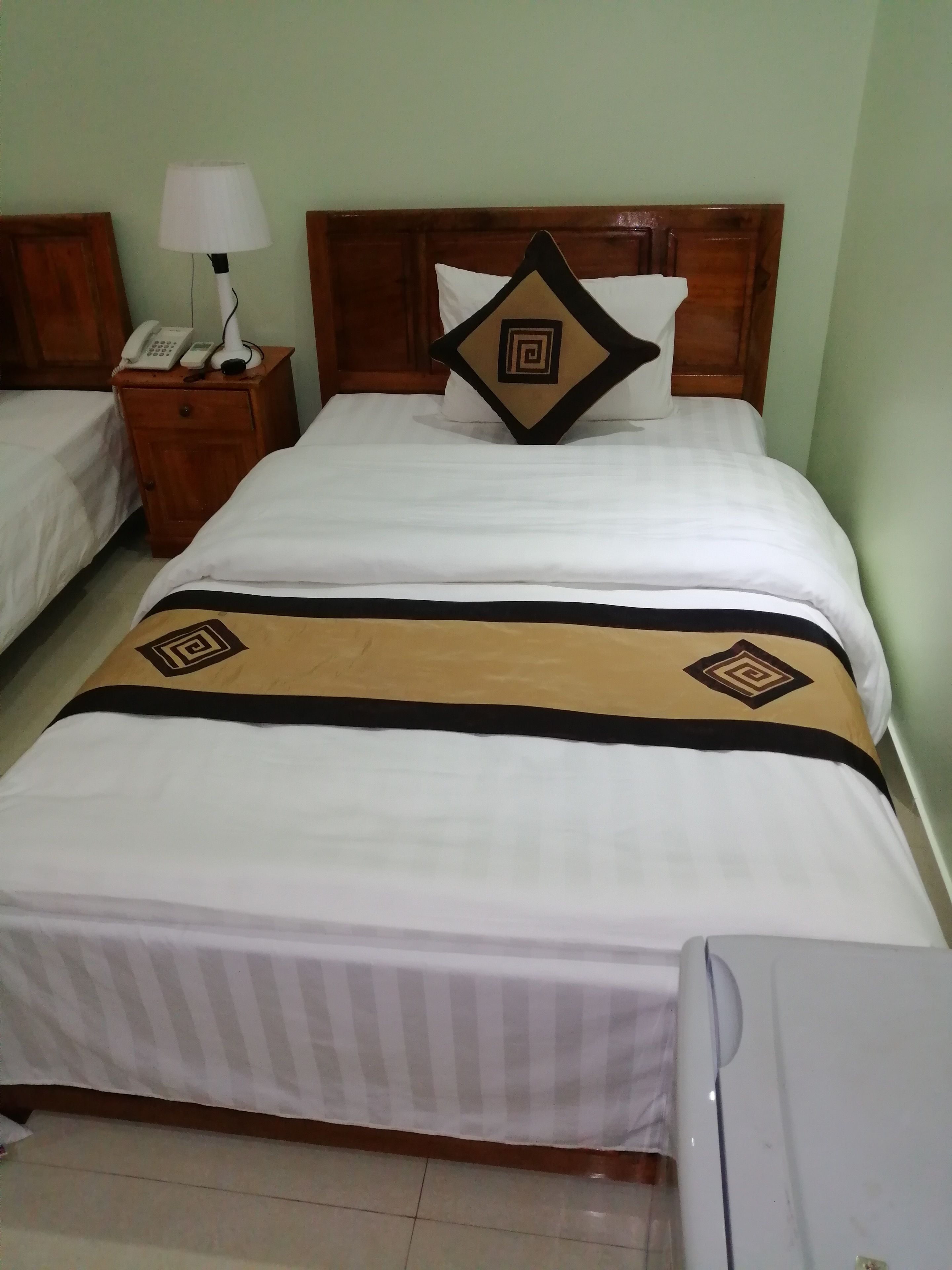 A neatly made bed with a patterned bedspread, a bedside lamp, and a telephone on a wooden nightstand.