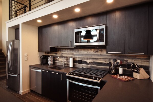 A modern kitchen with dark wood cabinets, stainless steel appliances, and a built-in microwave. - The Salida Opera House Loft (Salida)