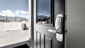 A door with a keypad lock and a view of a mountainous landscape through a window. - The Salida Opera House Loft (Salida)